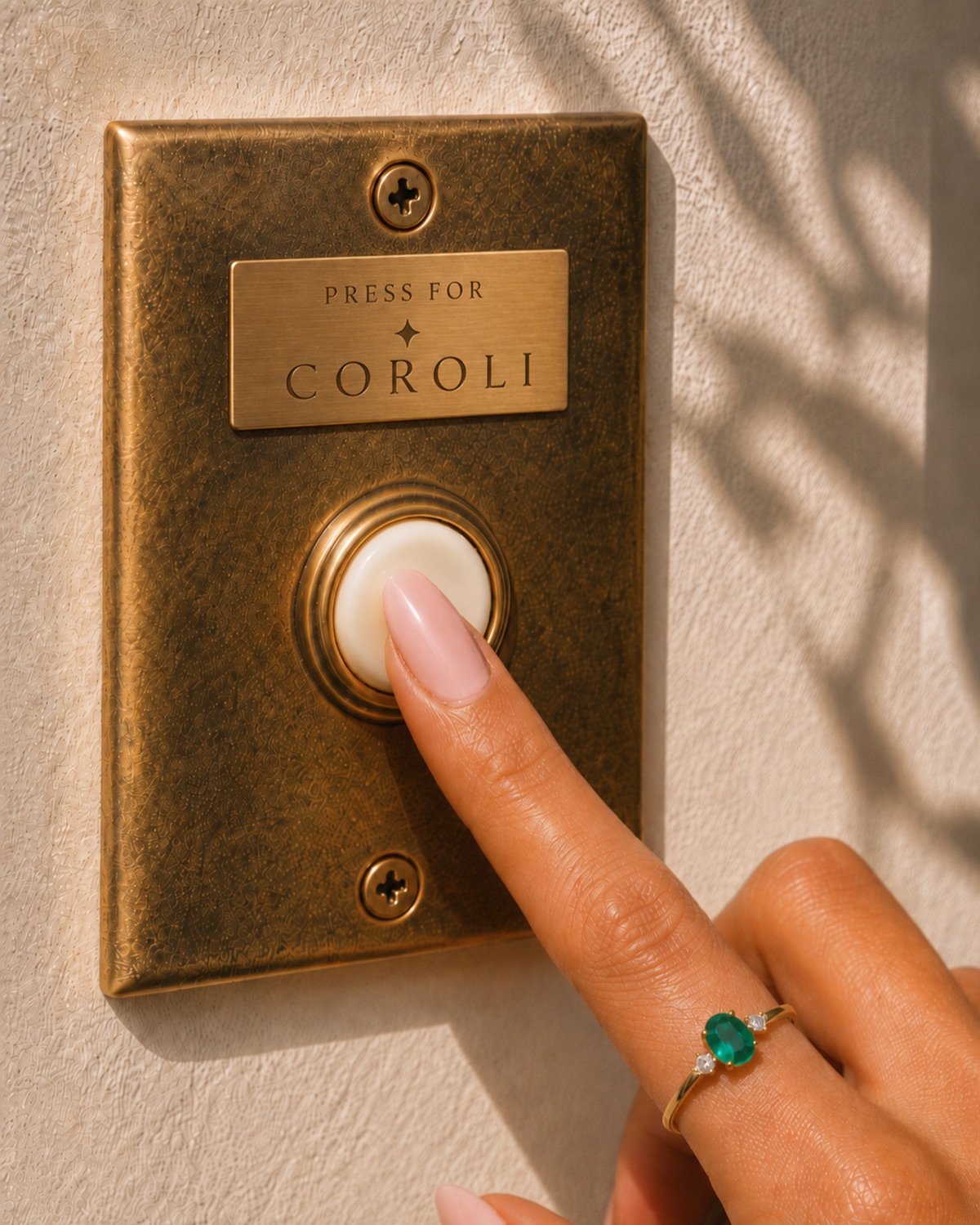 Dedo com o anel de esmeralda Coroli apertando uma campainha de latão com a placa Press for Coroli